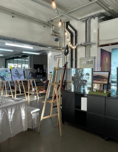 Des tableaux exposés sur des chevalets, avec des tables dressées en arrière-plan